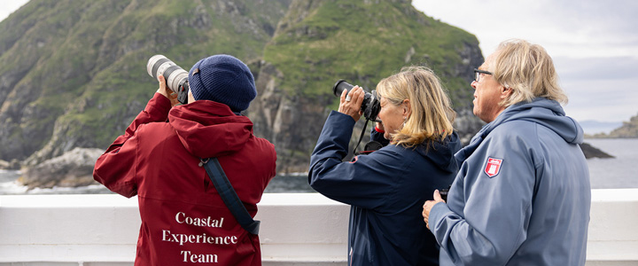 landingpage_Hurtigruten_Galerie_02_20250722 12 Tage Expeditionsreise inkl. Flug mit Hurtigruten in Norwegen. Drei Menschen mit Ferngläsern erkunden die Natur Norwegens vom Schiff aus.