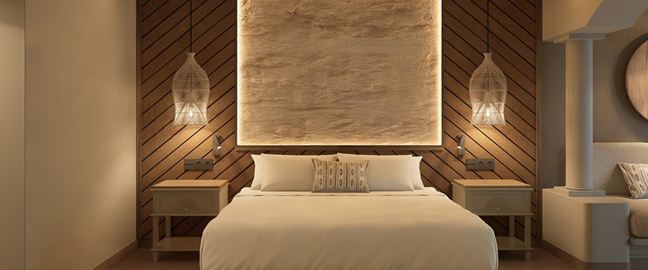 Hotelzimmer mit Fokus auf ein Bett, gehalten in Braun- und Beigetönen, stimmungsvolles Licht lädt zum Entspannen ein.