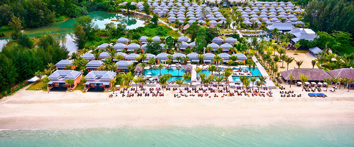 Weiter Sandstrand mit Villen, Pools und Liegeflächen, umgeben von einer tropischer Palmenlandschaft, die zum Entspannen einlädt.