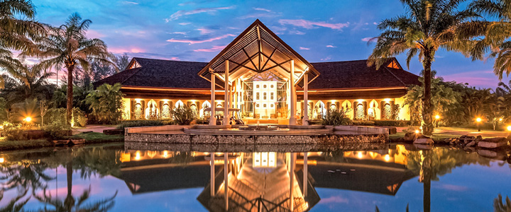Luxuriöses Resort, umgeben von Palmen und Wasser, Spiegelungen im Wasser bei stimmungsvollem Abendlicht.