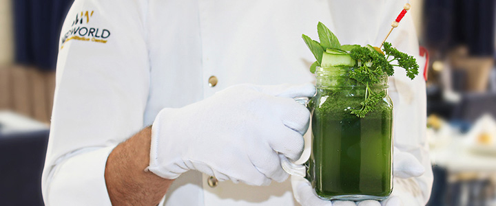 Koch von Medworld hält einen leuchtend grünen, gesunden Smoothie in der Hand.