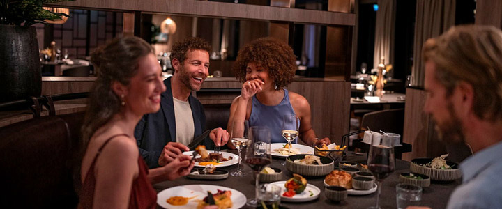 Eine Gruppe von Freunden sitzt in einem stilvollen Restaurant, lacht und genießt gemeinsam mehrere Gänge in entspannter Atmosphäre – ein Abend voller Genuss und Geselligkeit.