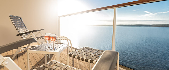 Zwei Liegestühle und Gläser mit Getränken stehen auf einem sonnigen Balkon mit Blick auf das ruhige Meer und laden zu entspannten Momenten an Bord ein.