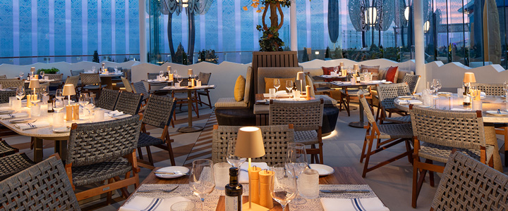 Celebrity Xcel; gemütliches Restaurant mit Meerblick, angenehme Atmosphäre bei sanfter Beleuchtung.