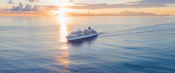 Kreuzfahrtschiff von Hapag Lloyd Cruises auf offenem Meer in rotlicher Abendstimmung.