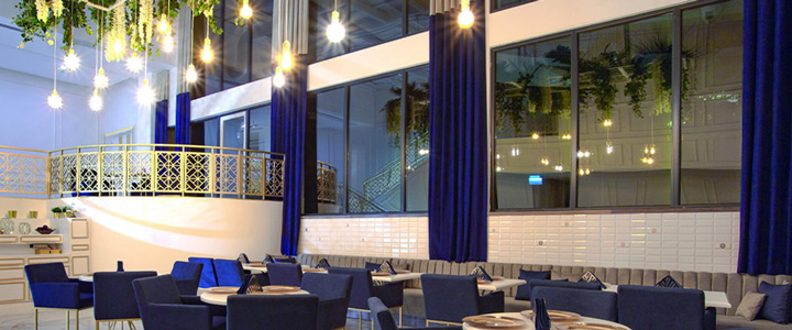 Elegantes Restaurant, im Fokus stehen Tische mit blauen Stühlen und blauen Vorhängen an den Fenstern, angenehme Beleuchtung.