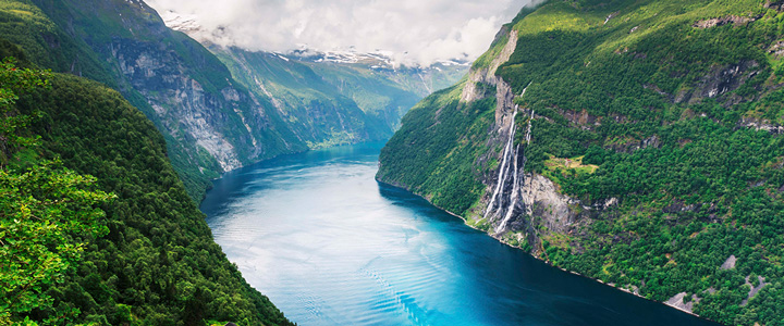 Ruhiges Gewässer im Fokus, umgeben von Bergen mit frischem Grün bei schönem Wetter.