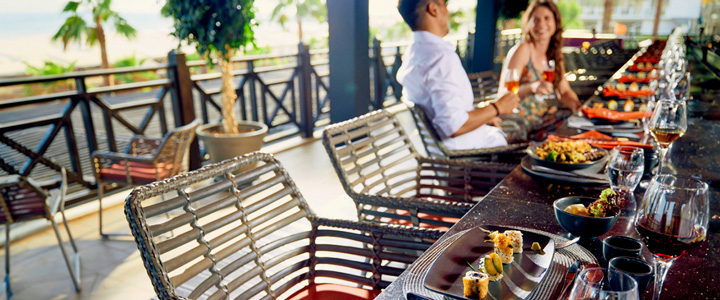 Sonnendurchflutetes Restaurant, Tisch und Stühle im Vordergrund; auf den Tellern frisch angerichtetes Sushi, während im Hintergrund Personen sitzen.