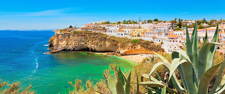 Typischer portugisischer Küstenort auf einer Steilküste gelegen mit dem türkisblauen Meer, weißem Strand und unberührter Natur im Vordergrund.