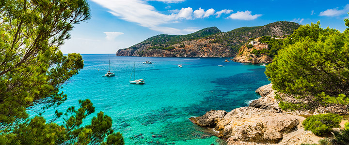 Blick in die idyllische Landschaft und auf das türkisblaue Meer mit Segelschiffen vor der Mittelmeerküste.
