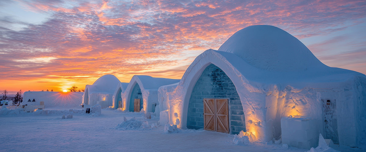Außergewöhnliche Reiseziele und Hotels gesucht? Das Bild zeigt ein Eishotel in Lappland, gebaut aus Schnee und Eis in märchenhafter Kulisse im Abendrot.