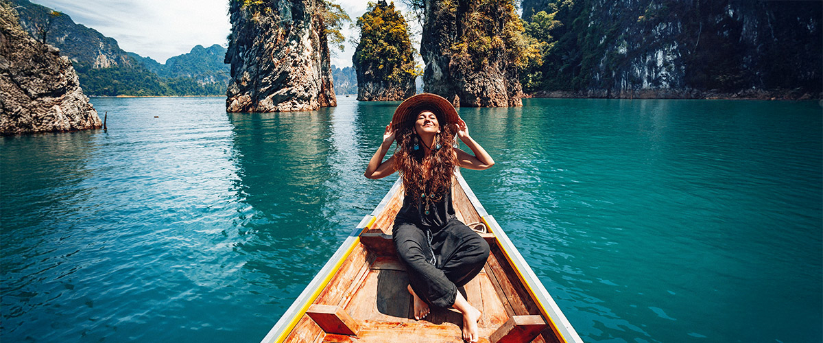 Junge Frau genießt die Sonne und die atemberaubende Natur bei ihrer induviduell geplanten Rundreise in Thailand auf einem typischen Boot.