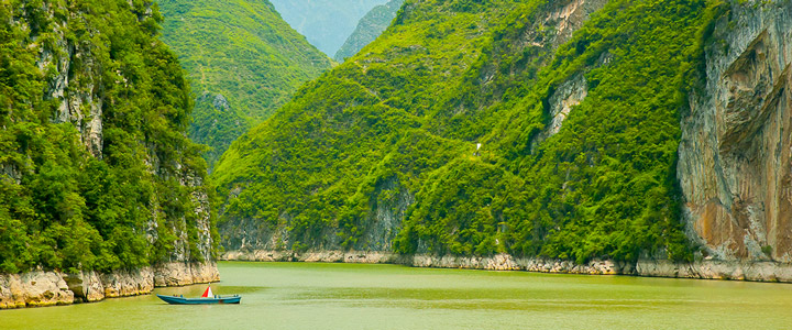 Grüne Oase am Yangtze mit einem Boot auf dem Wasser, umgeben von bewaldeten Felsen in einem tiefen Tal. Links und rechts ragen hohe Berge auf.