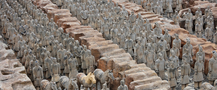 Blick von oben auf die Terrakotta-Armee in Xi’an mit dicht gereihten Statuen, die sich eindrucksvoll über das Areal verteilen.