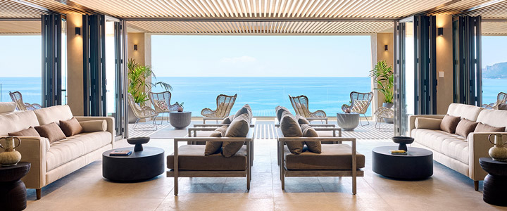 Das Ella Álkyna zeigt einen stilvoll gestalteten Loungebereich in warmen Brauntönen mit offener Architektur und weitem Blick auf das Meer.