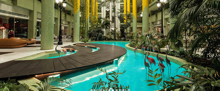 Stilvollen Innenbereich mit tropischem Flair. Ein geschwungener Wasserlauf mit kleinen Brücken, Palmen und dekorativen Flamingos zieht sich durch die lichtdurchflutete Lobby. Hohe Säulen.