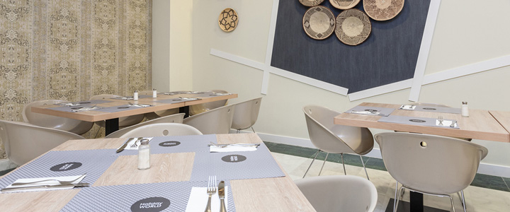 Das Bild zeigt einen hellen, stilvoll eingerichteten Restaurantbereich im Holiday World Riwo Hotel. Der Raum ist mit Esstischen in heller Holzoptik und modernen, beigefarbenen Schalenstühlen ausgestattet.