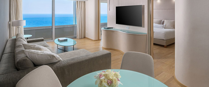 Helle Suite im Rodos Palace mit großzügigem Wohnbereich und direktem Meerblick. Ein breiter Balkon öffnet sich zur Küste.