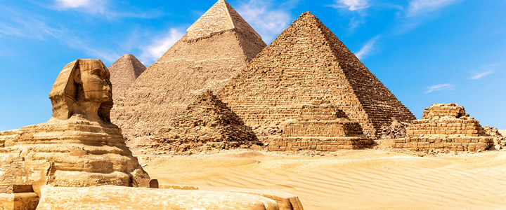 Die Sphinx wacht vor den Pyramiden von Gizeh, eingebettet in die weite Wüstenlandschaft. Goldenes Licht betont die monumentale Szenerie des alten Ägyptens.
