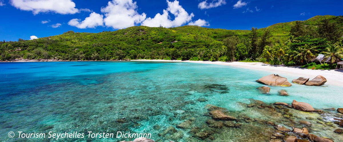 Die Anse Takamaka auf Mahé zeigt eine idyllische Bucht mit türkisblauem Meer, weißem Sandstrand und üppiger tropischer Vegetation.
